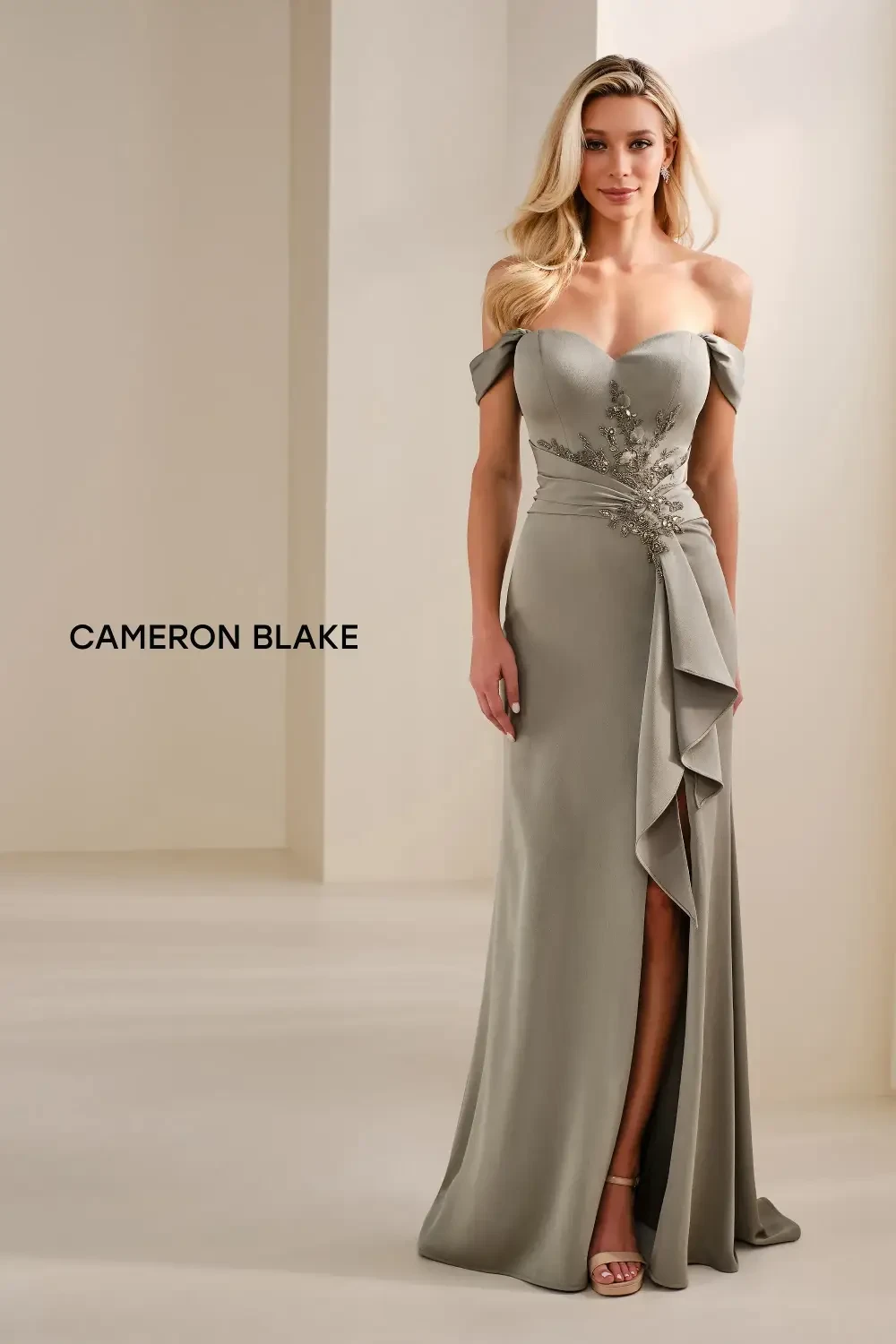 A woman wearing an elegant off-the-shoulder gown with a fitted silhouette and a thigh-high slit, standing in a bright, neutral-toned setting.