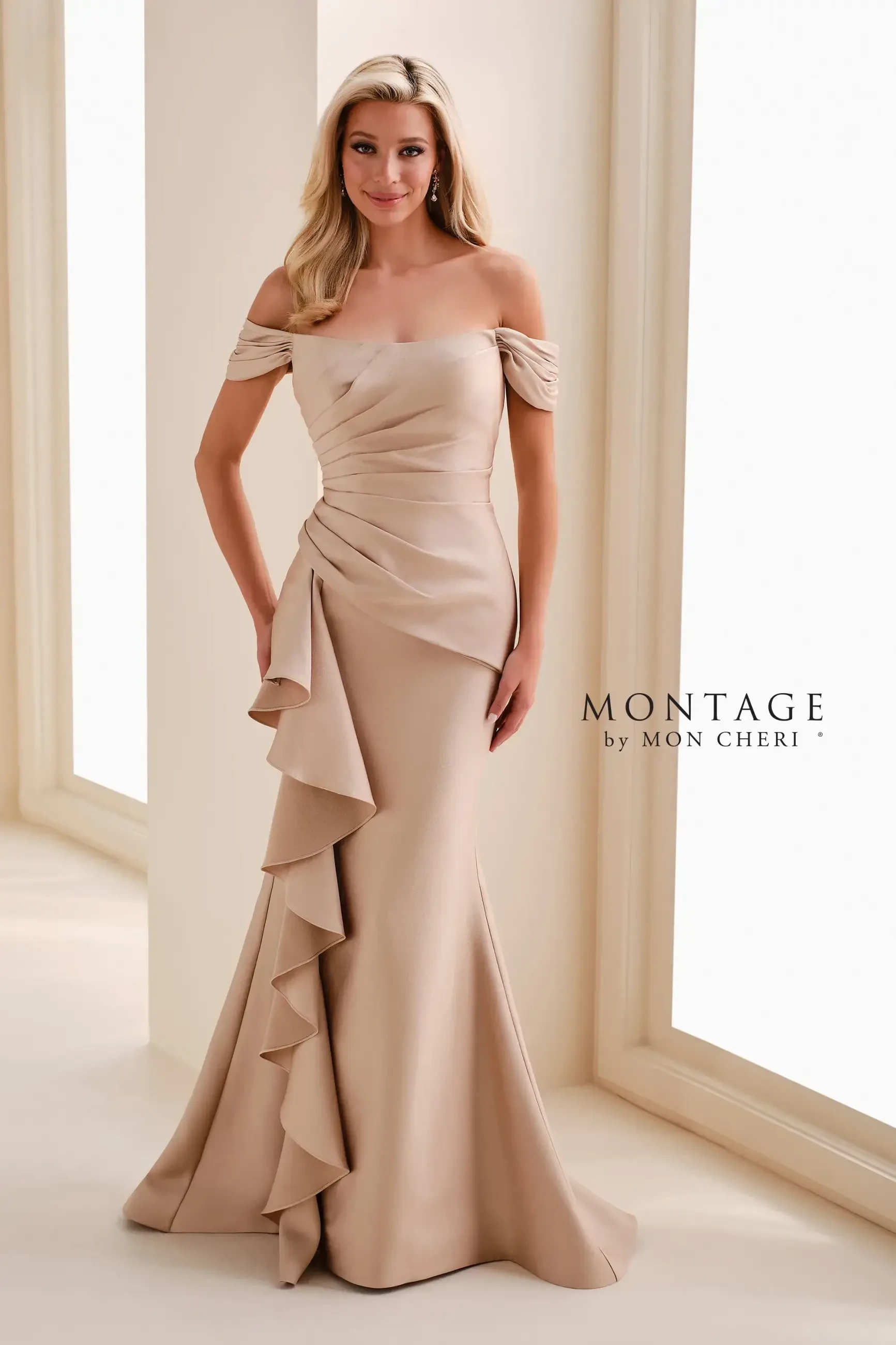 A woman in a formal off-the-shoulder gown with draped fabric and ruffles, standing in a well-lit area.