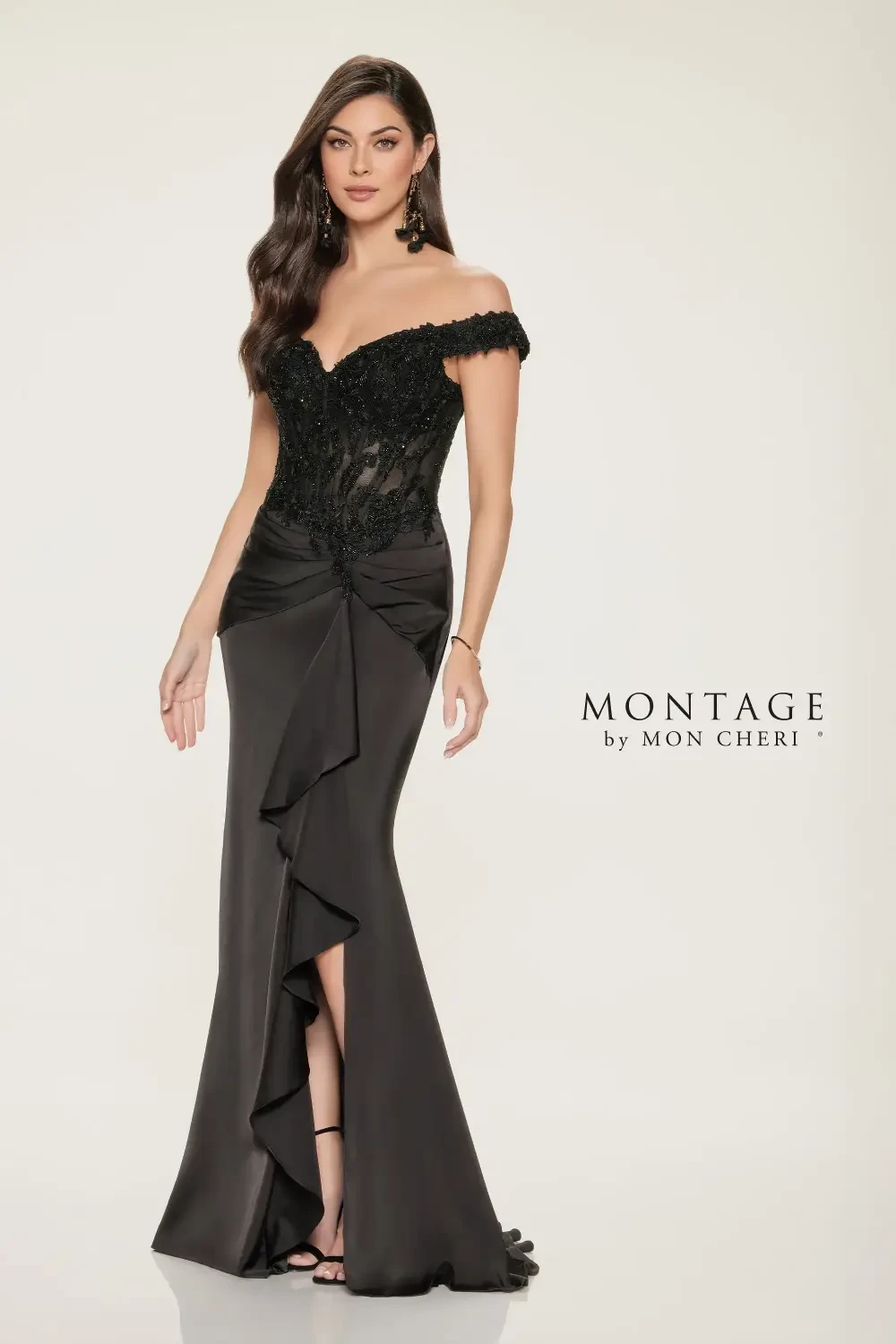 A model wearing a black evening gown with off-the-shoulder lace detailing and a ruffled skirt, standing elegantly.